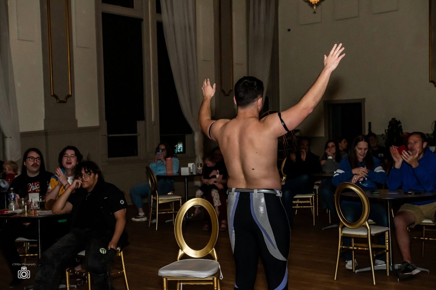 A wrestler raises both arms to a seated ballroom audience