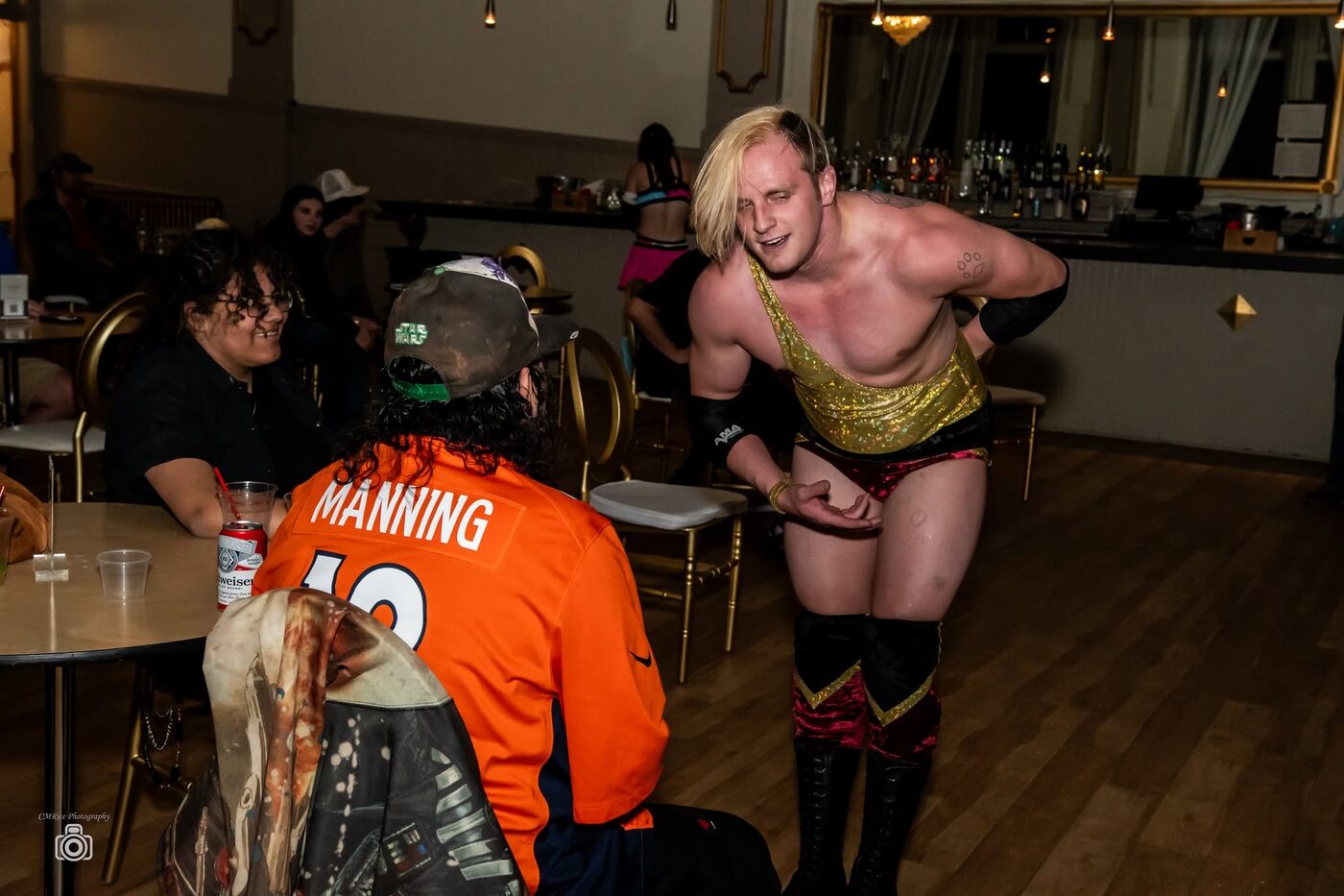 A wrestler leans over a ringside table of seated fans