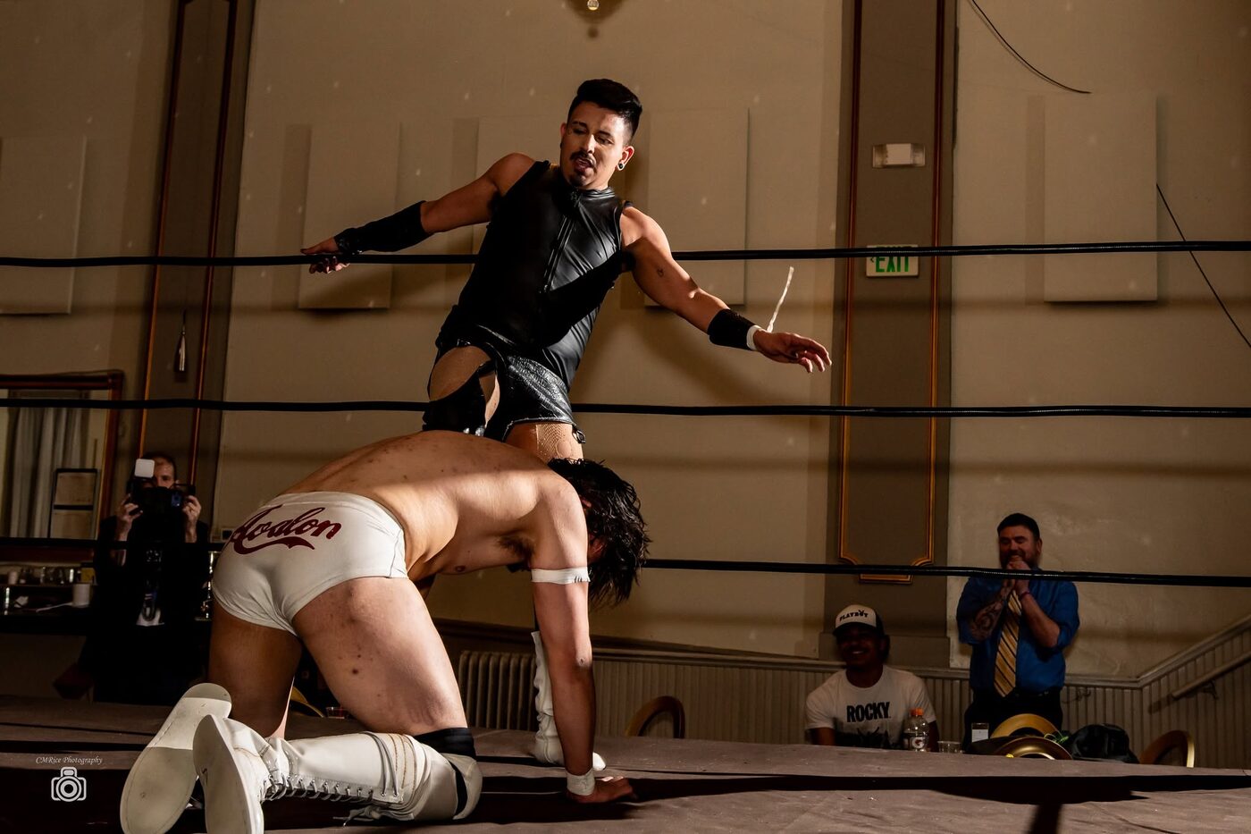 A wrestler leaps over a kneeling opponent as the crowd watches