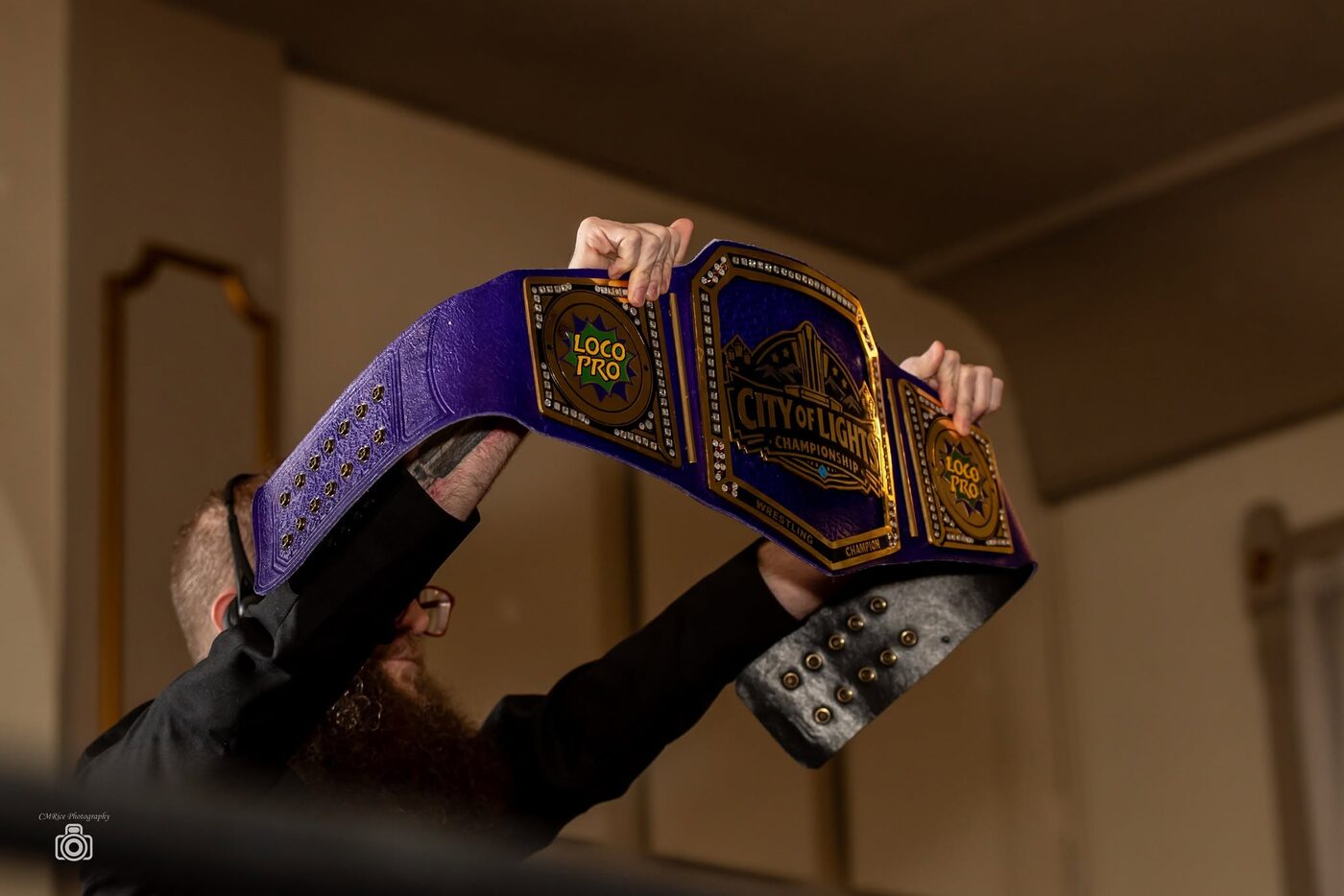 A wrestler holds the City of Lights Championship belt overhead