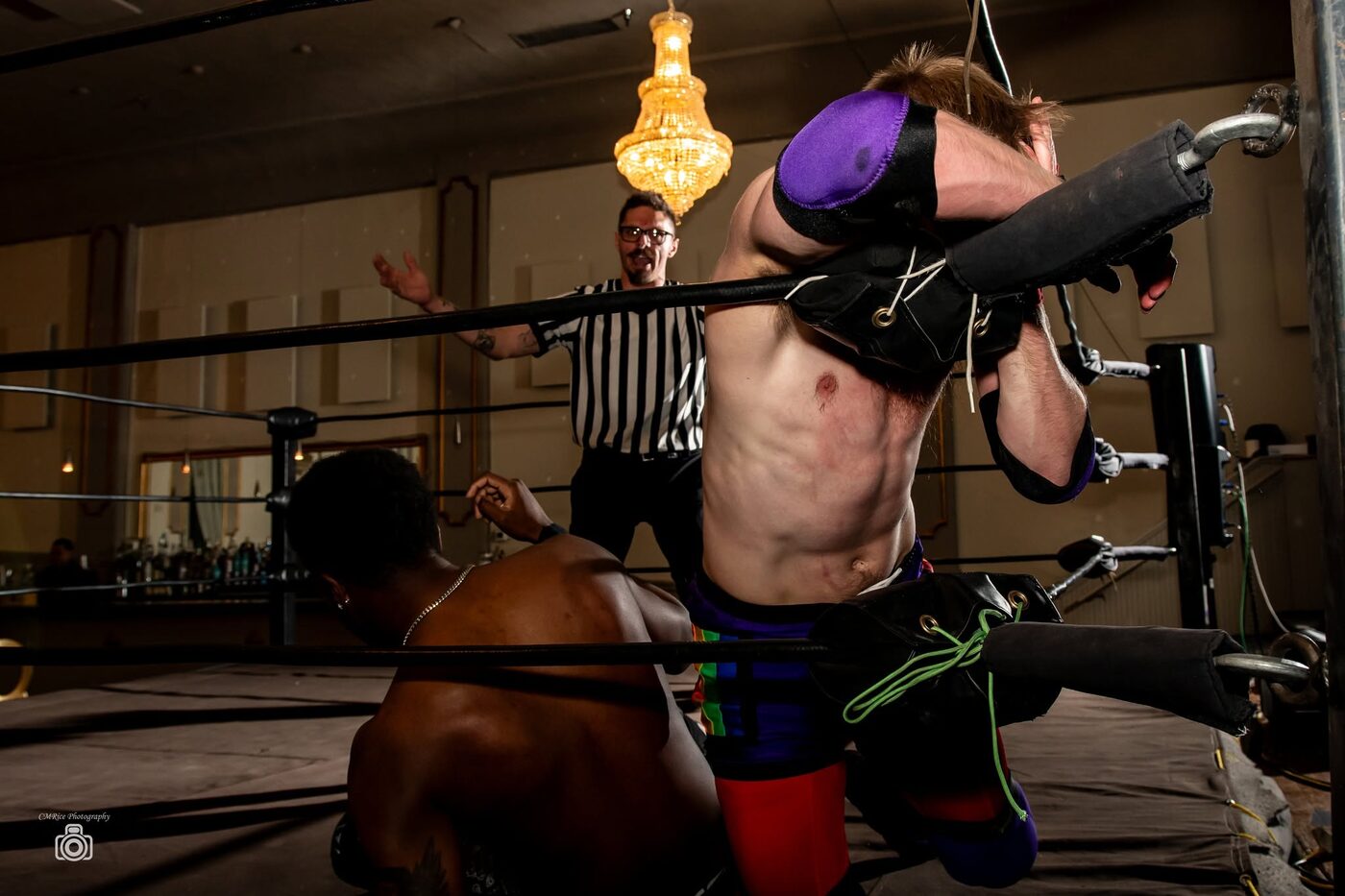 A wrestler lifted across the ropes as the referee signals