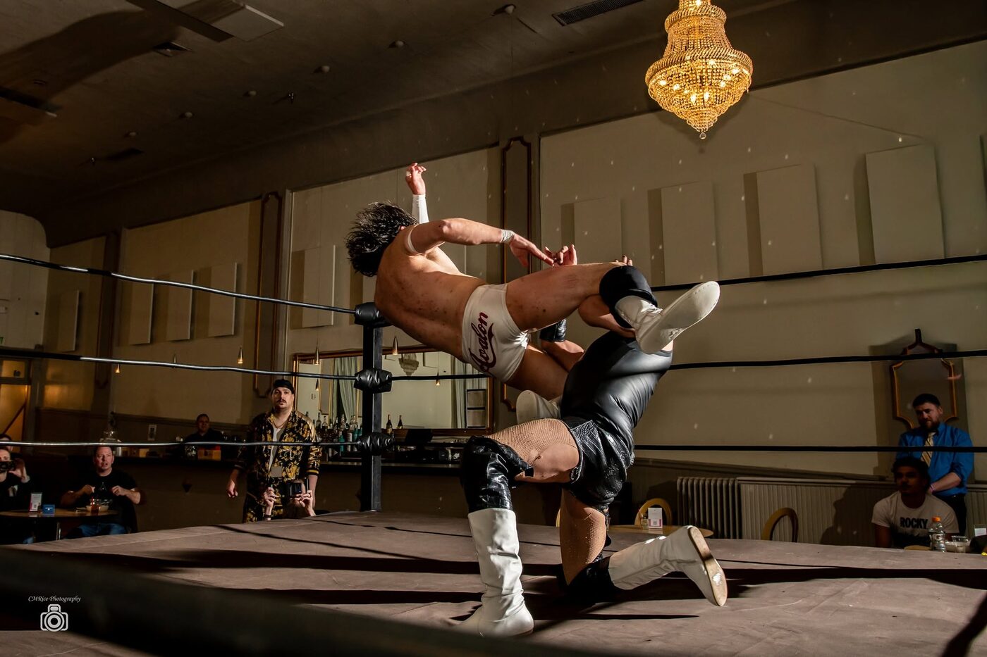 A wrestler mid-air above the ring beneath a chandelier